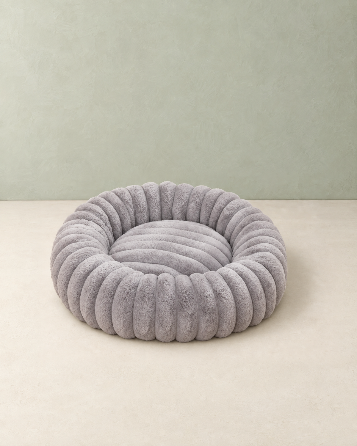 Round light grey donut dog bed in ribbed plush with a padded centre, on a cream floor against a pale sage wall
