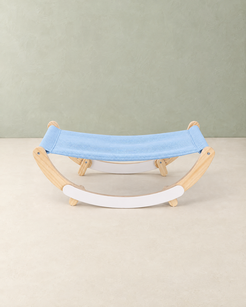 Cat hammock bed with a light blue mesh sling on a pale wooden frame with white rockers, on a cream floor