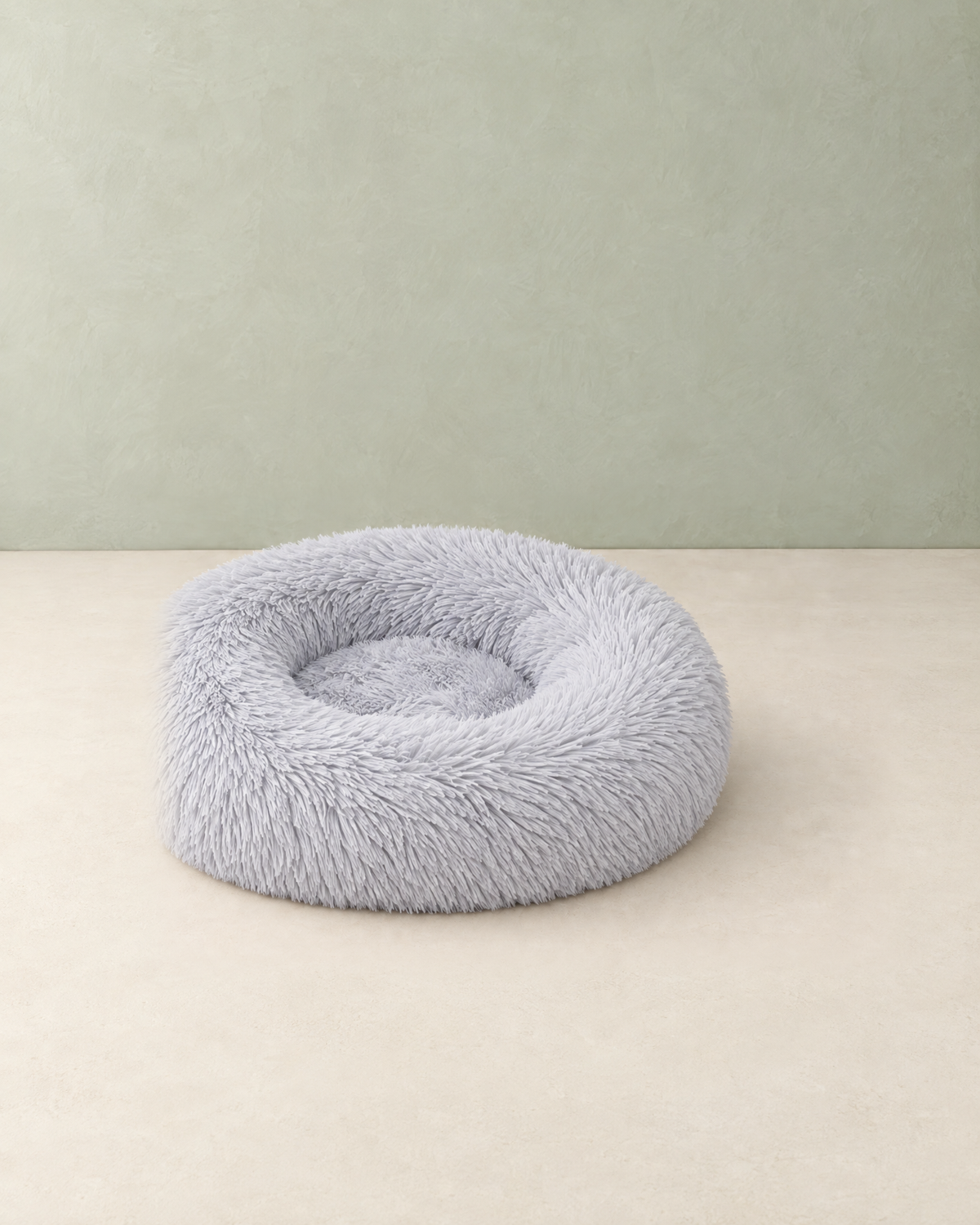 Light grey round fluffy donut cat bed on a cream floor against a pale sage wall