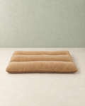 Camel curly-fleece dog bed cushion with three padded rolls, lying flat on a cream floor against a pale sage wall