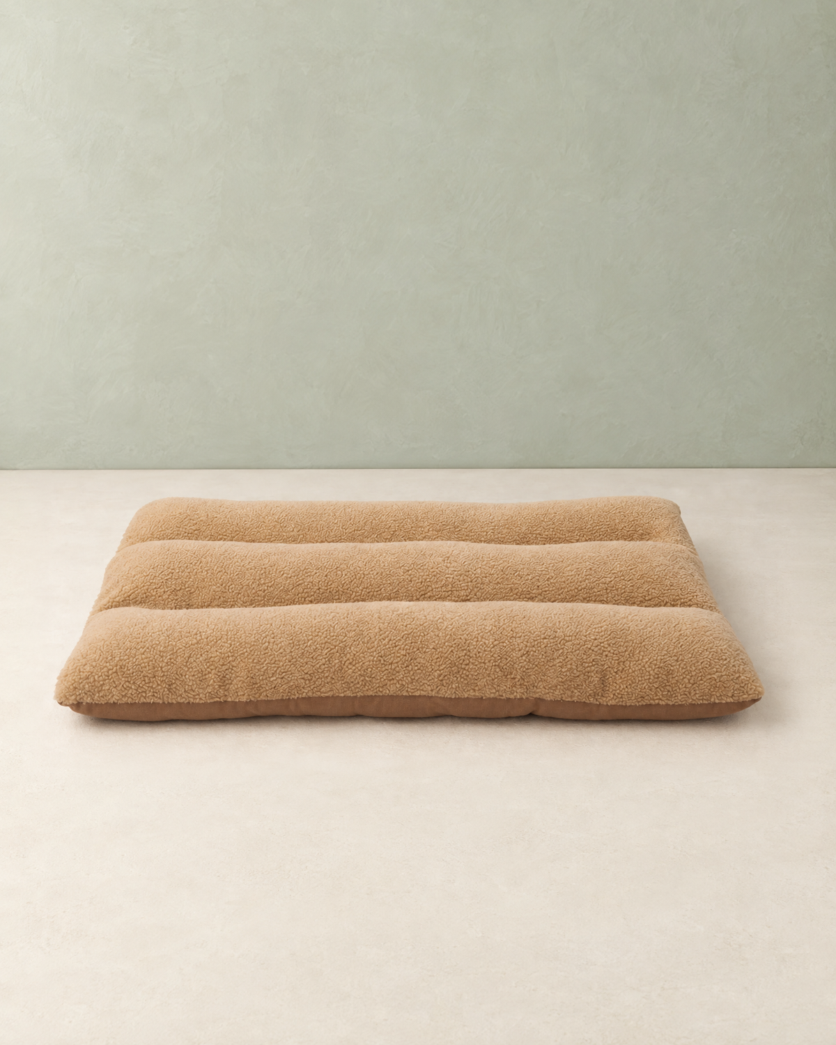 Camel curly-fleece dog bed cushion with three padded rolls, lying flat on a cream floor against a pale sage wall
