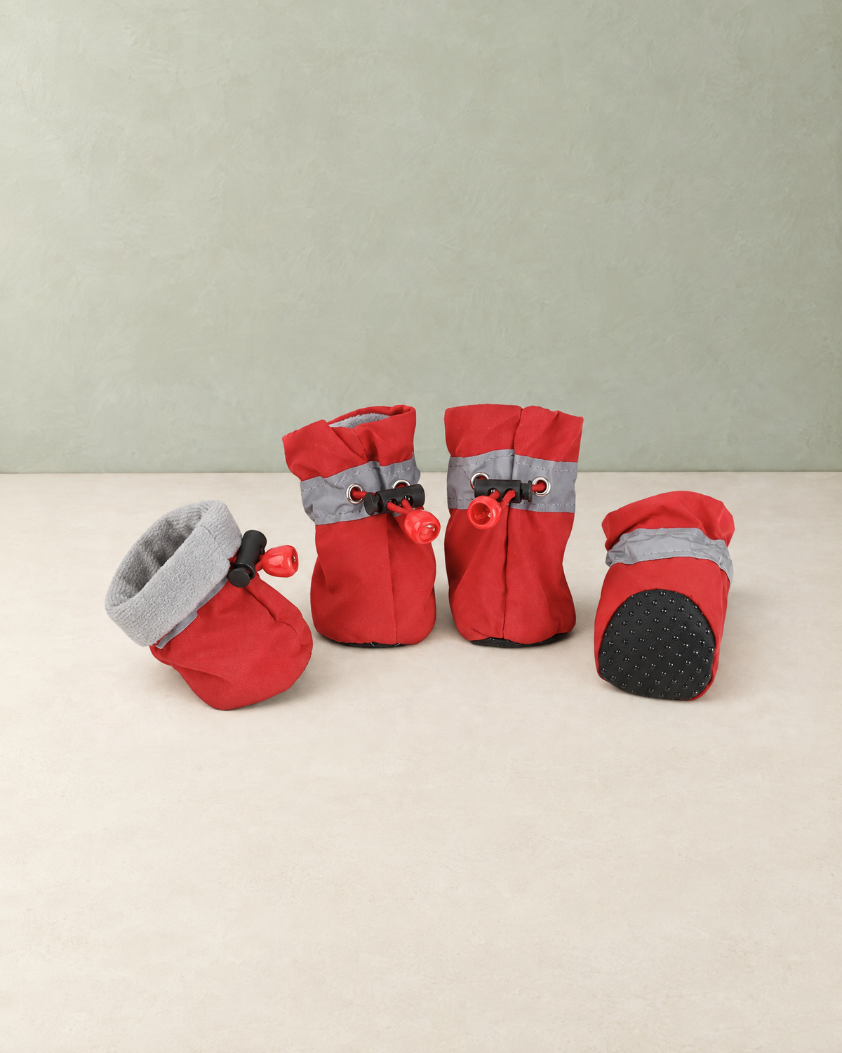 Four red fleece-lined dog boots with grey reflective bands and drawstring toggles, one showing its dotted non-slip sole