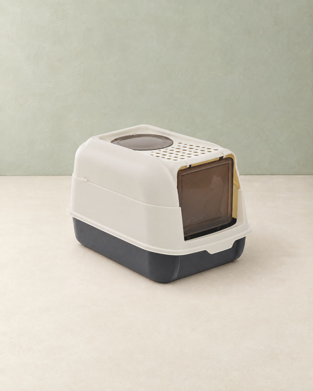 Cream and charcoal hooded cat litter box with a tinted front flap door and a round top entry, on a cream floor against a pale sage wall