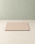 Beige curly-fleece self-warming pet mat lying flat on a cream floor against a pale sage wall