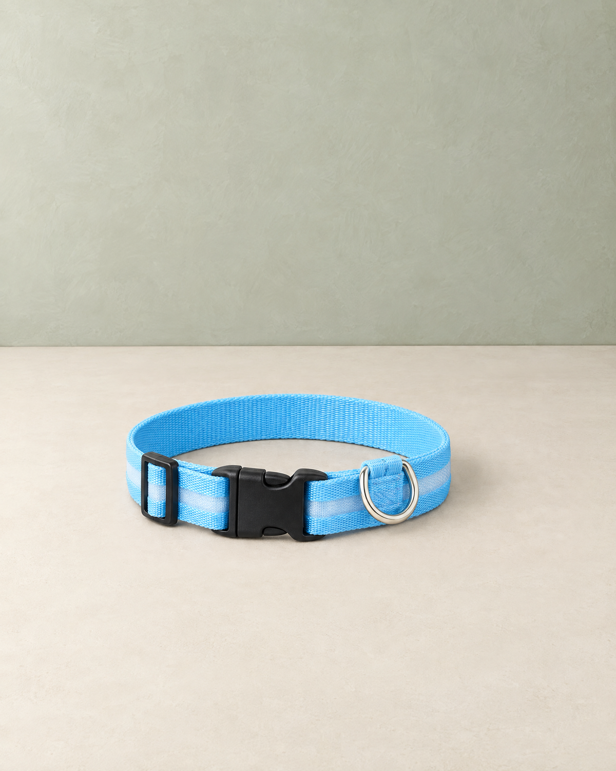Sky-blue LED dog collar with a pale light stripe, black side-release buckle and silver D-ring, lying on a cream floor