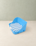 Blue small-pet litter tray with a high back and a white removable grid, on a cream floor against a pale sage wall