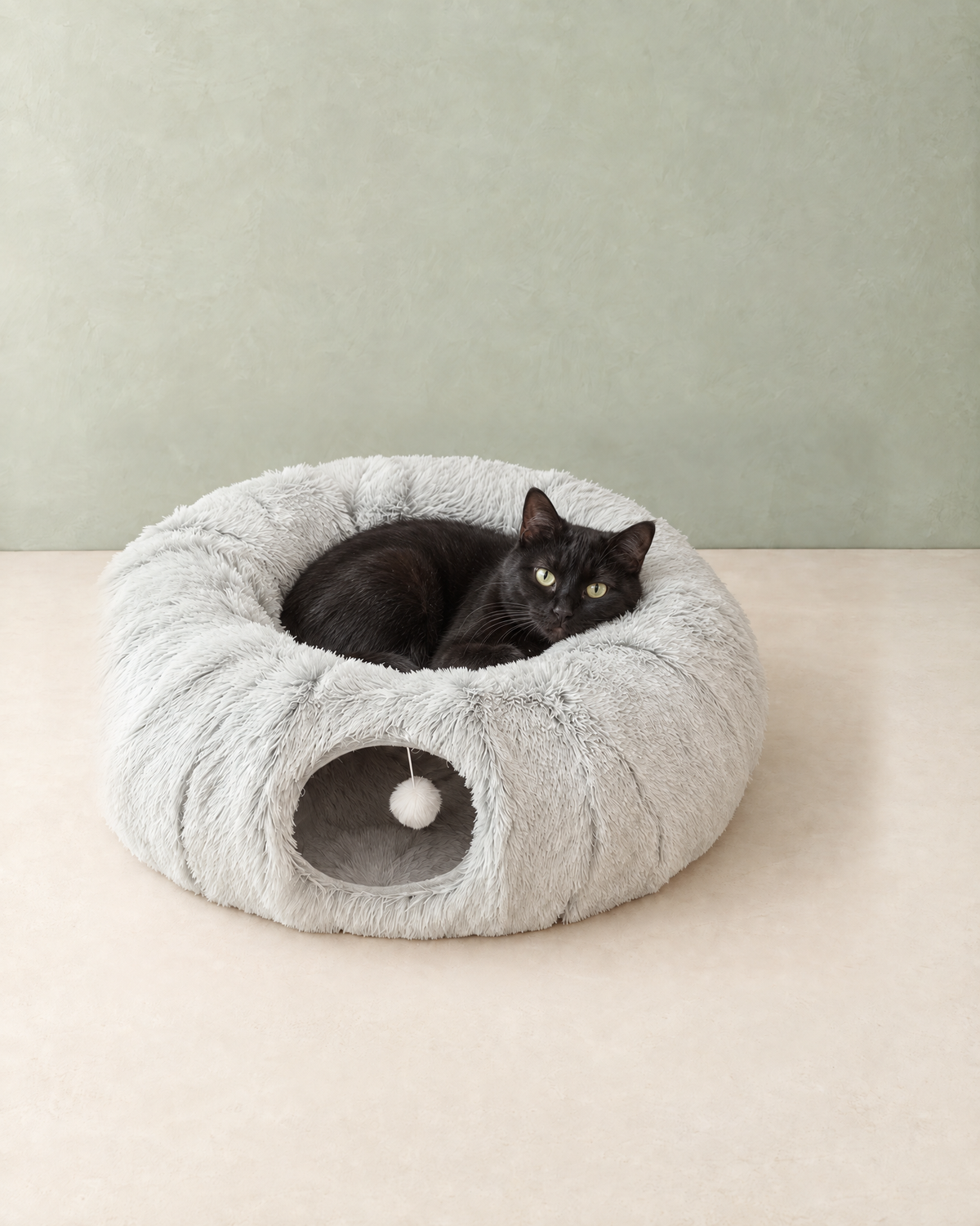A black cat curled up in the middle of the light grey plush cat tunnel bed