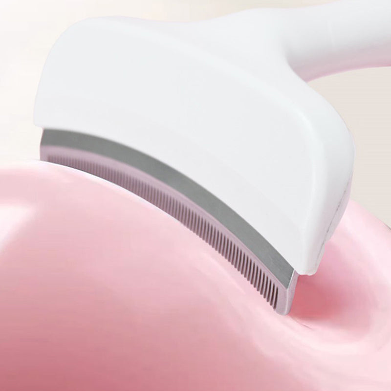 The deshedding comb resting on a pink cushion, its curved steel blade in view