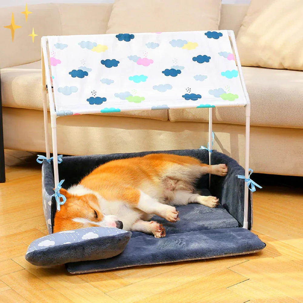 A corgi asleep on the navy fleece mat of the dog bed with its front folded down under a cloud-print roof